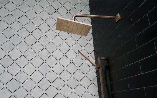 Brushed gold shower fixtures mounted on matte black subway tile and white marble patterned tile in a Herndon, VA bathroom remodel.