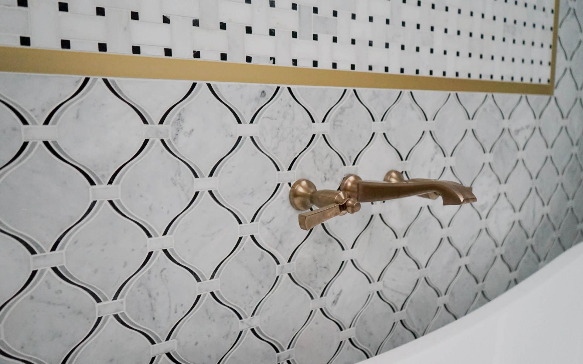 Brushed gold shower fixtures mounted on matte black subway tile and white marble patterned tile in a Herndon, VA bathroom remodel.