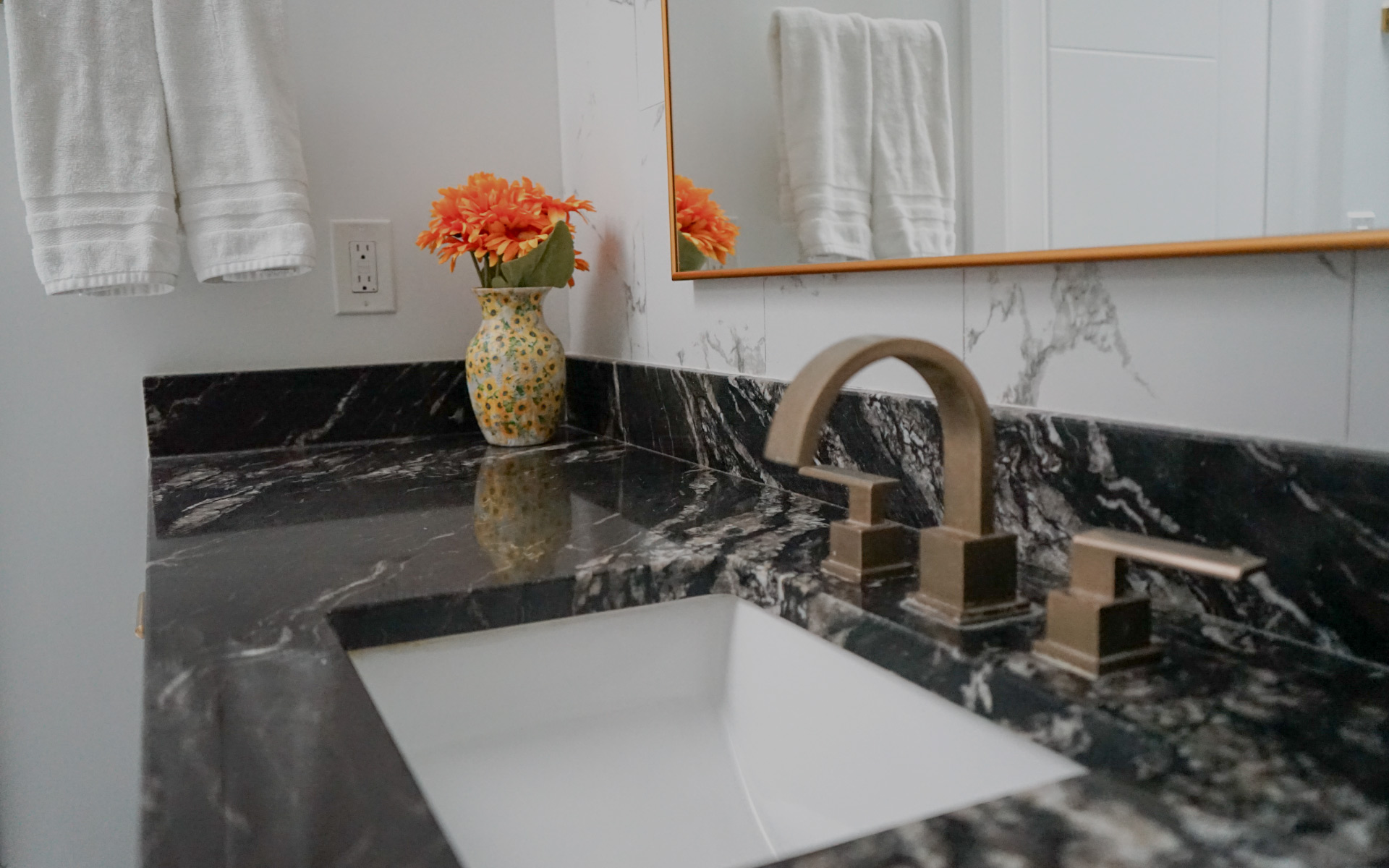 Close-up of a black marble vanity countertop with a brushed gold faucet and undermount sink in a Herndon, VA bathroom remodel.
