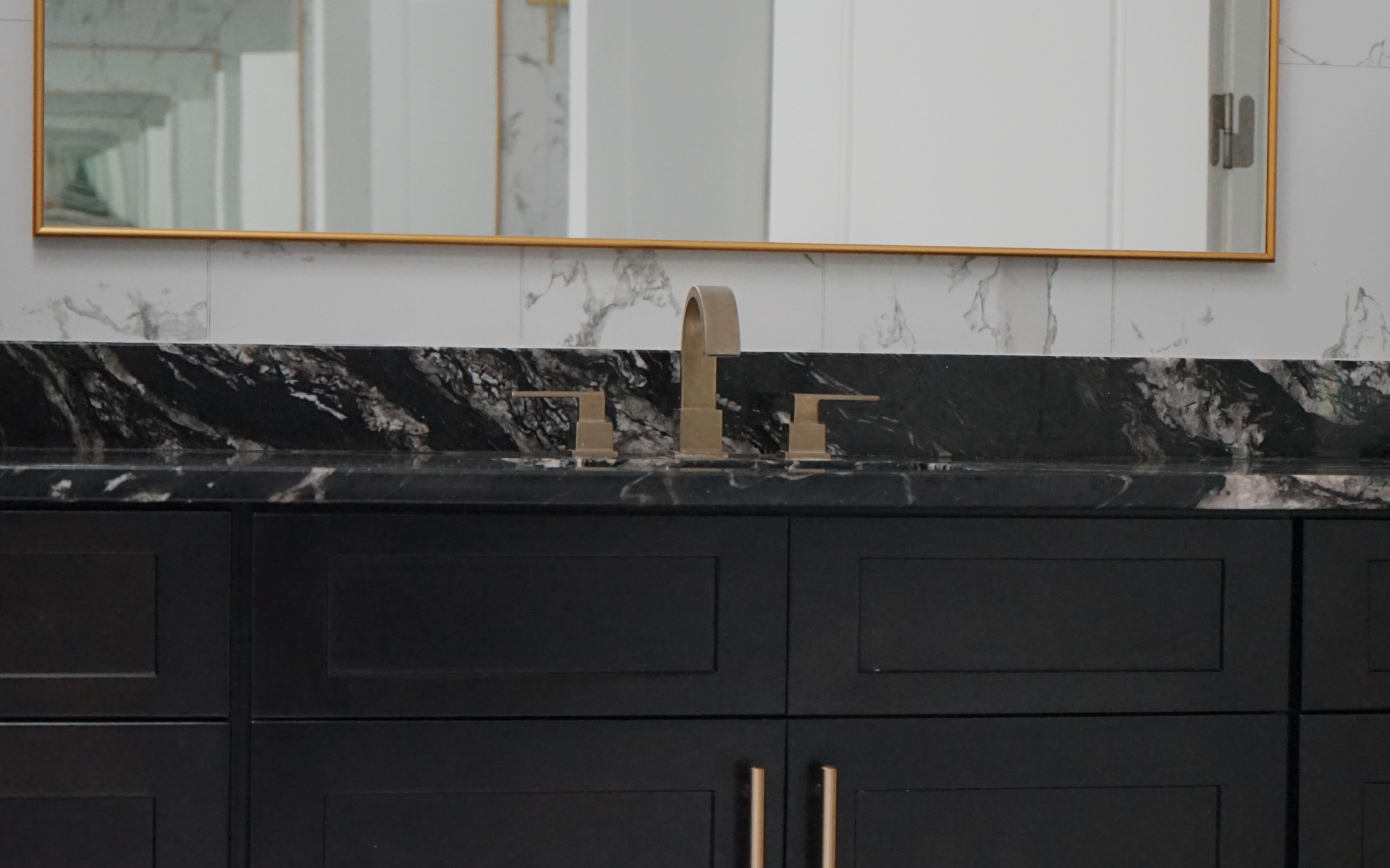 Close-up of a black marble vanity countertop with a brushed gold faucet and undermount sink in a Herndon, VA bathroom remodel.