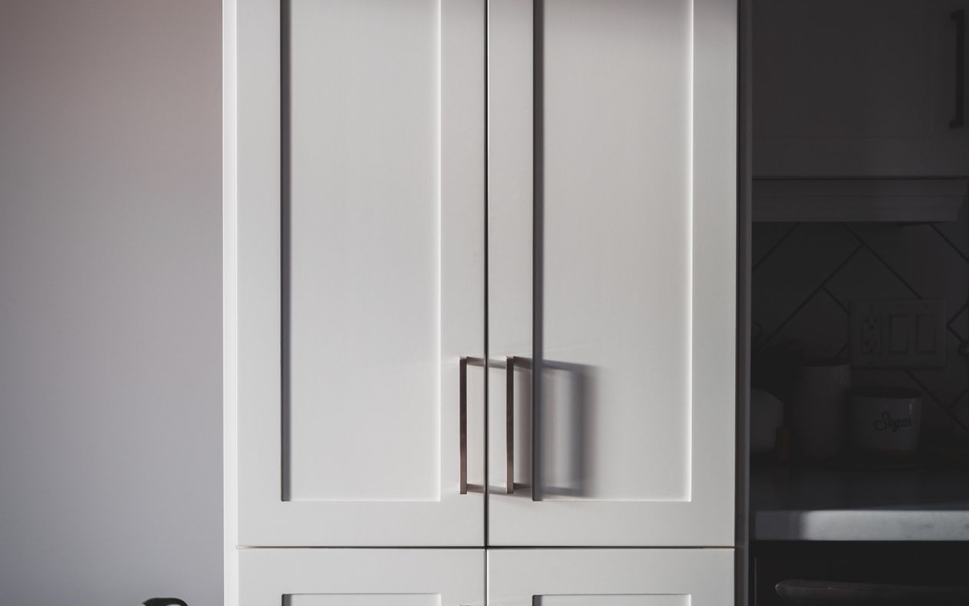 A close-up shot of white shaker-style kitchen cabinets with dark rectangular metal handles.